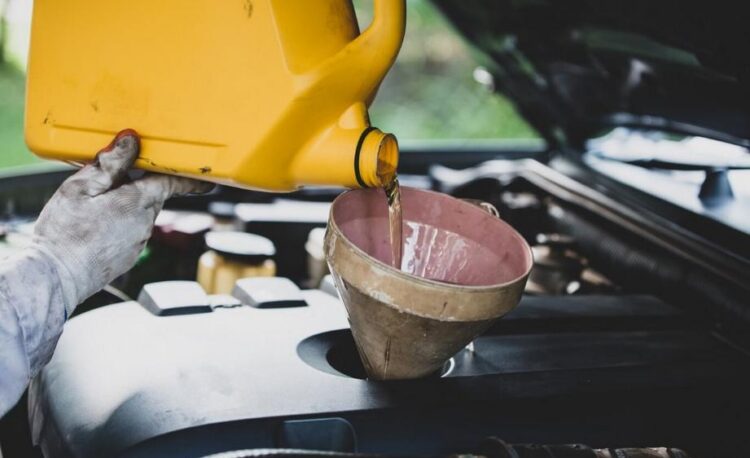 a car mechanic hand-pouring fresh oil in a car